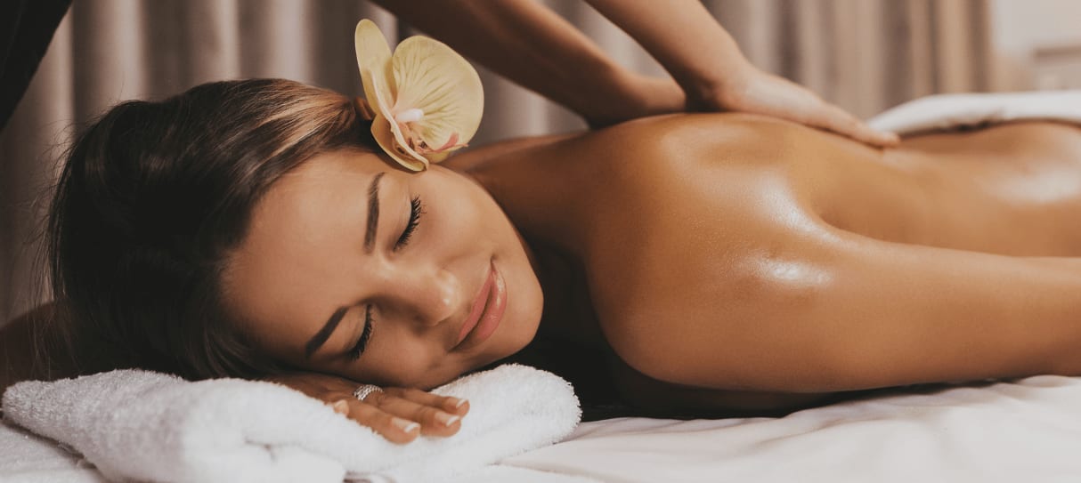 Frau mit Orchidee im Haar genießt eine entspannende Ganzkörpermassage