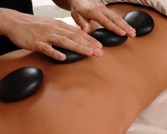 Hände legen warme Basaltsteine für eine Hot-Stone-Massage auf den Rücken