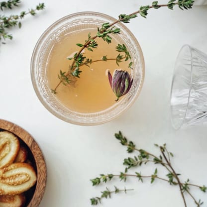 Kräutergetränk mit Thymianzweig und Blüte, dazu kleine Snacks