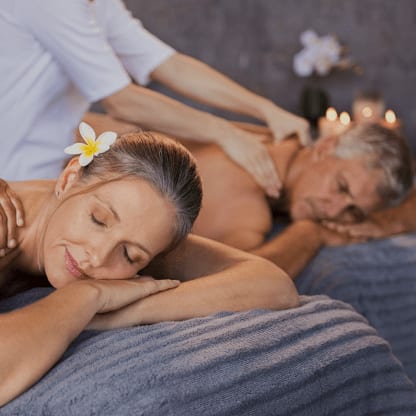 Ein reiferes Paar genießt gemeinsam eine Massage bei Kerzenschein, eine Blüte im Haar der Frau