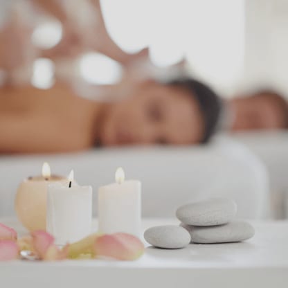 Brennende Kerzen und Massagesteine, im Hintergrund ein entspanntes Paar