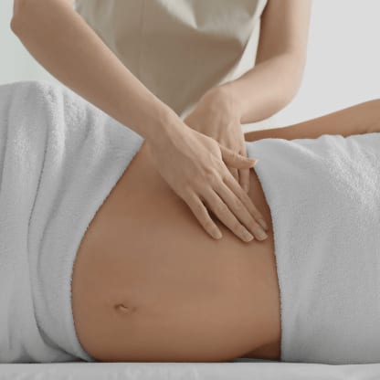 Sanfte Massage im Taillen- und Hüftbereich einer schwangeren Gästin, in ein Handtuch gehüllt