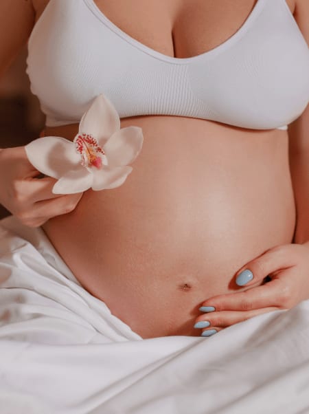 Nahaufnahme des Babybauchs einer werdenden Mutter, die eine Orchideenblüte in der Hand hält